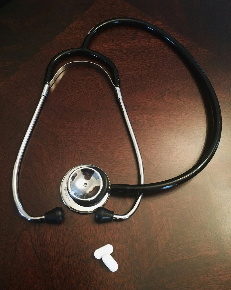 A stethoscope on a table with two medical pills